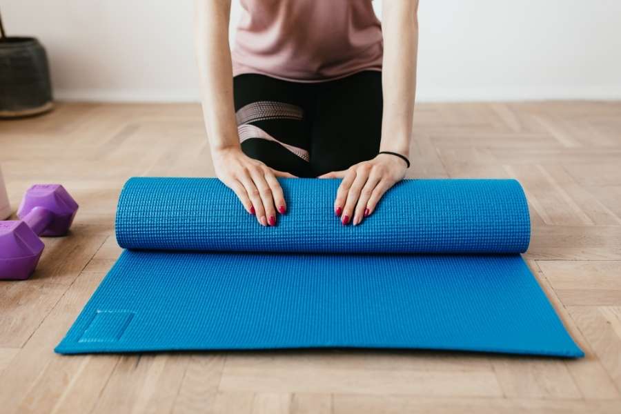 Une personne enroule soigneusement son tapis de yoga bleu après une séance d'entraînement à domicile.