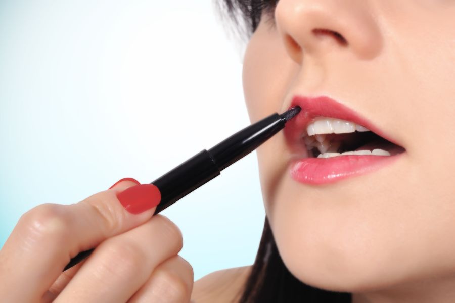 Une main utilise un pinceau pour dessiner et maquiller le contour des lèvres avec soin